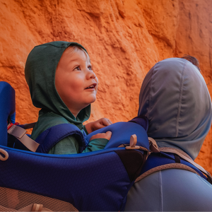 Child in a blue carrier with a person against a red rock background
