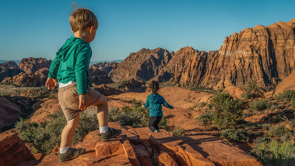 Two children exploring a desert landscape with red rock formations.