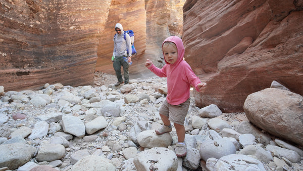 Child in pink jacket walking on rocky terrain with adult in the background