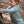 Child in a light hoodie romper standing next to a tree in a natural setting feeling the bark
