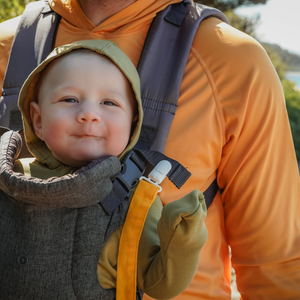 Baby in a carrier with a person wearing an orange jacket outdoors