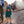 Child in a green hoodie walking on a rocky trail with a person and scenic landscape.